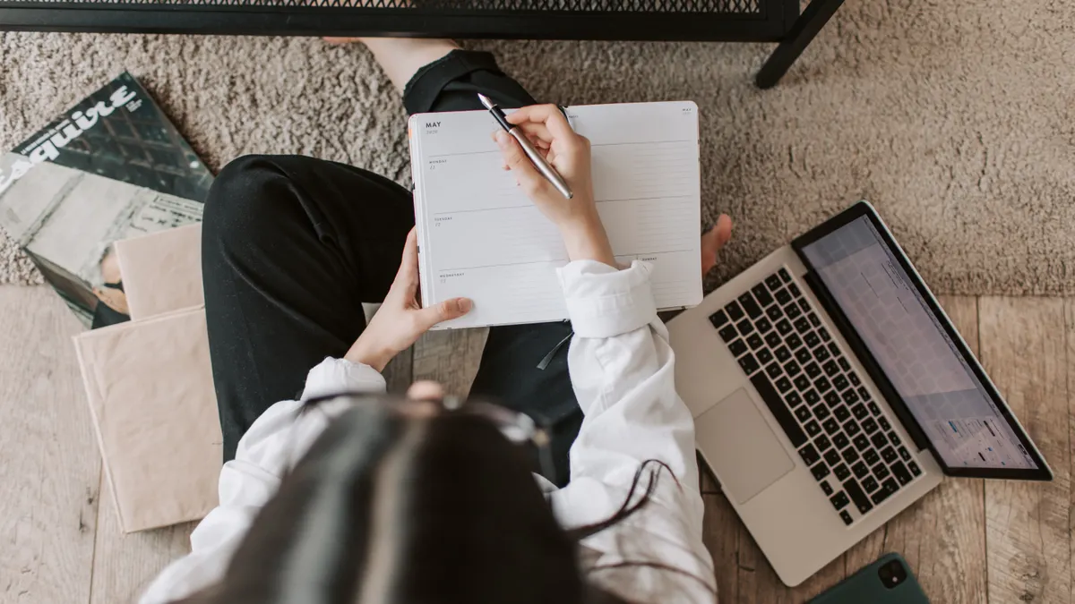 person planning in notebook beside a laptop