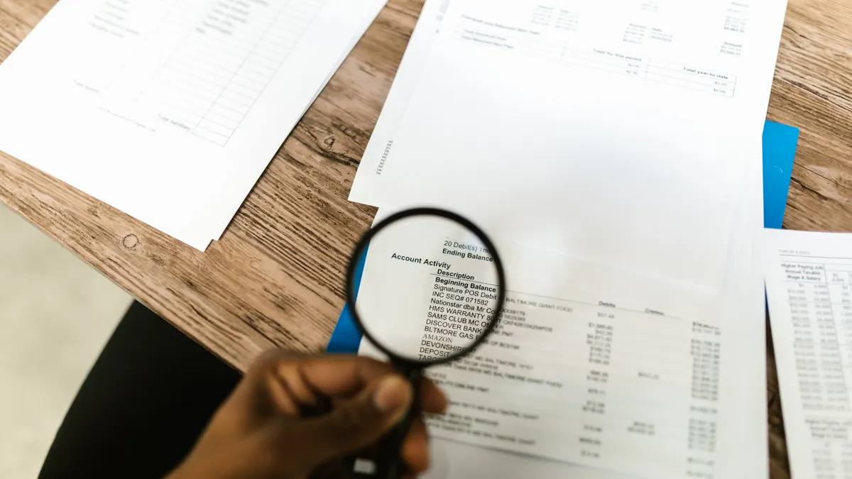 hand inspecting printed financial documents with a magnifying glass